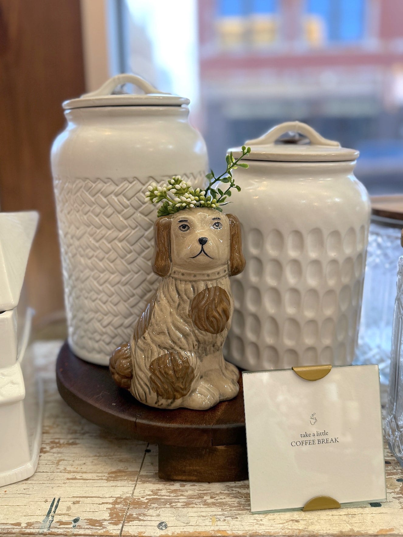 Brown and cream Staffordshire-style dog planter displayed with white textured canisters and greenery in warm lighting.