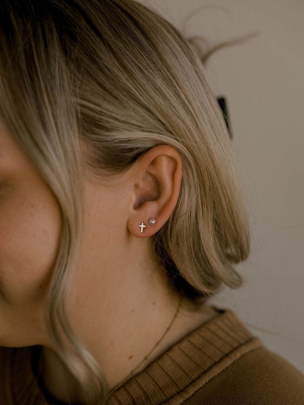 Woman wearing the Known Cross Earring Studs, showcasing the small gold cross on her ear.
