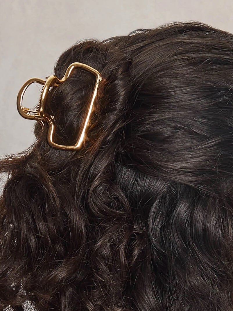 Medium puffy gold open claw clip securing brunette hair in a chic half-up style.
