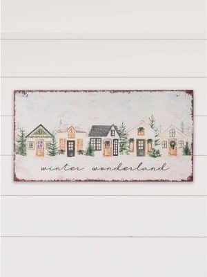 Rectangular metal wall sign featuring a painted row of colorful cottages in a snowy winter scene with evergreen trees and the words “winter wonderland.”