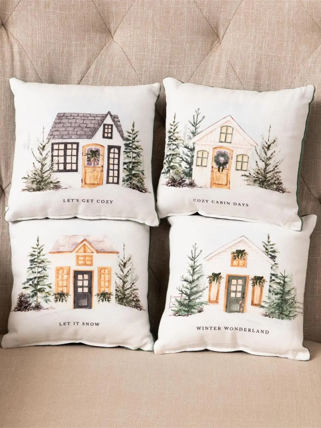 Small winter-themed pillow featuring an illustrated black-roofed cottage with pine trees and the phrase “Let’s Get Cozy.”