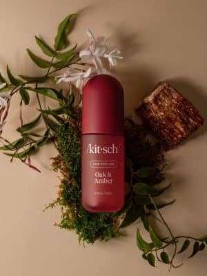 Kitsch Oak & Amber Hair Perfume bottle surrounded by greenery and wood accents.