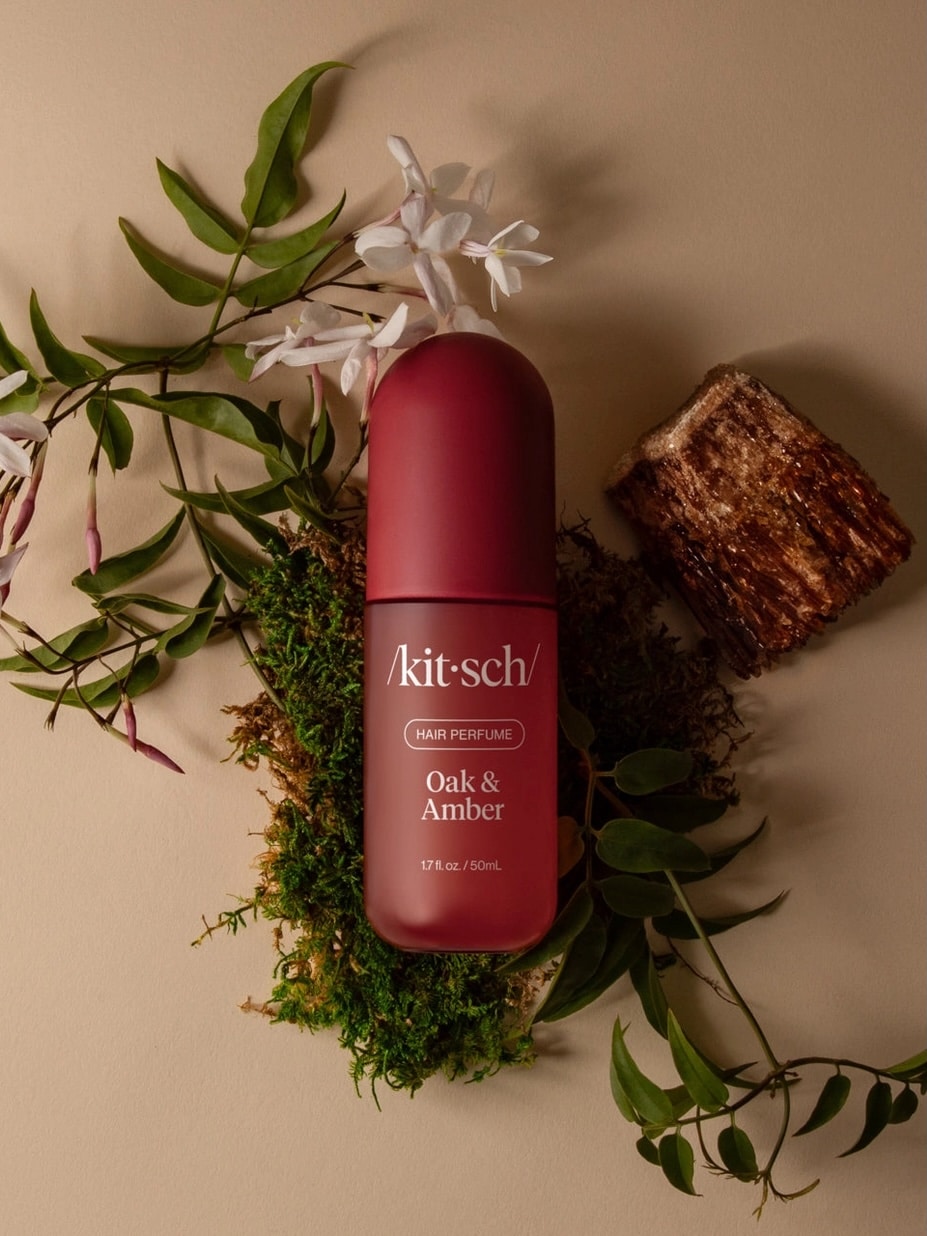 be-made-hays-ks-amber-wood-hair-fragrance Kitsch Oak & Amber Hair Perfume bottle surrounded by greenery and wood accents.