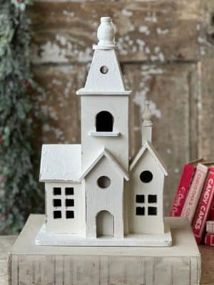 Distressed white chapel figurine with textured walls and classic gables styled in a vintage holiday setting.