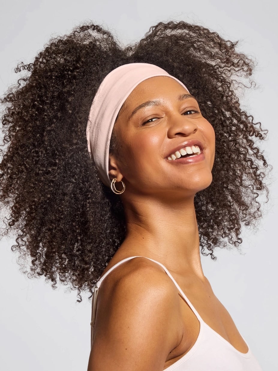 Woman with curly hair smiling while wearing a soft pink rosewood recycled headband.