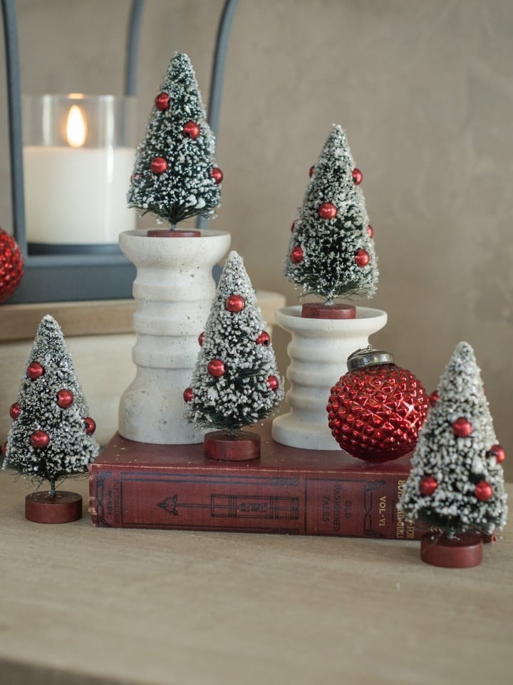 Mini Frosted Bottlebrush Trees styled on stacked books and pedestals with red ornaments and snow-dusted bristles for vintage Christmas decor.