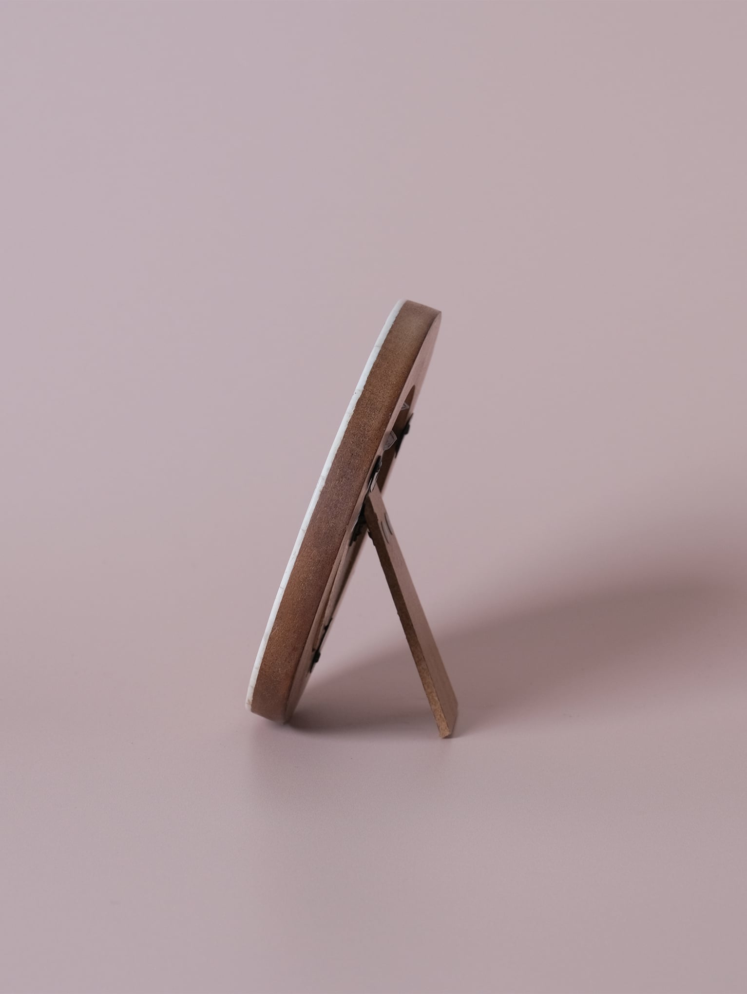 Side profile of round bone photo frame with easel back, shown standing on a neutral surface.
