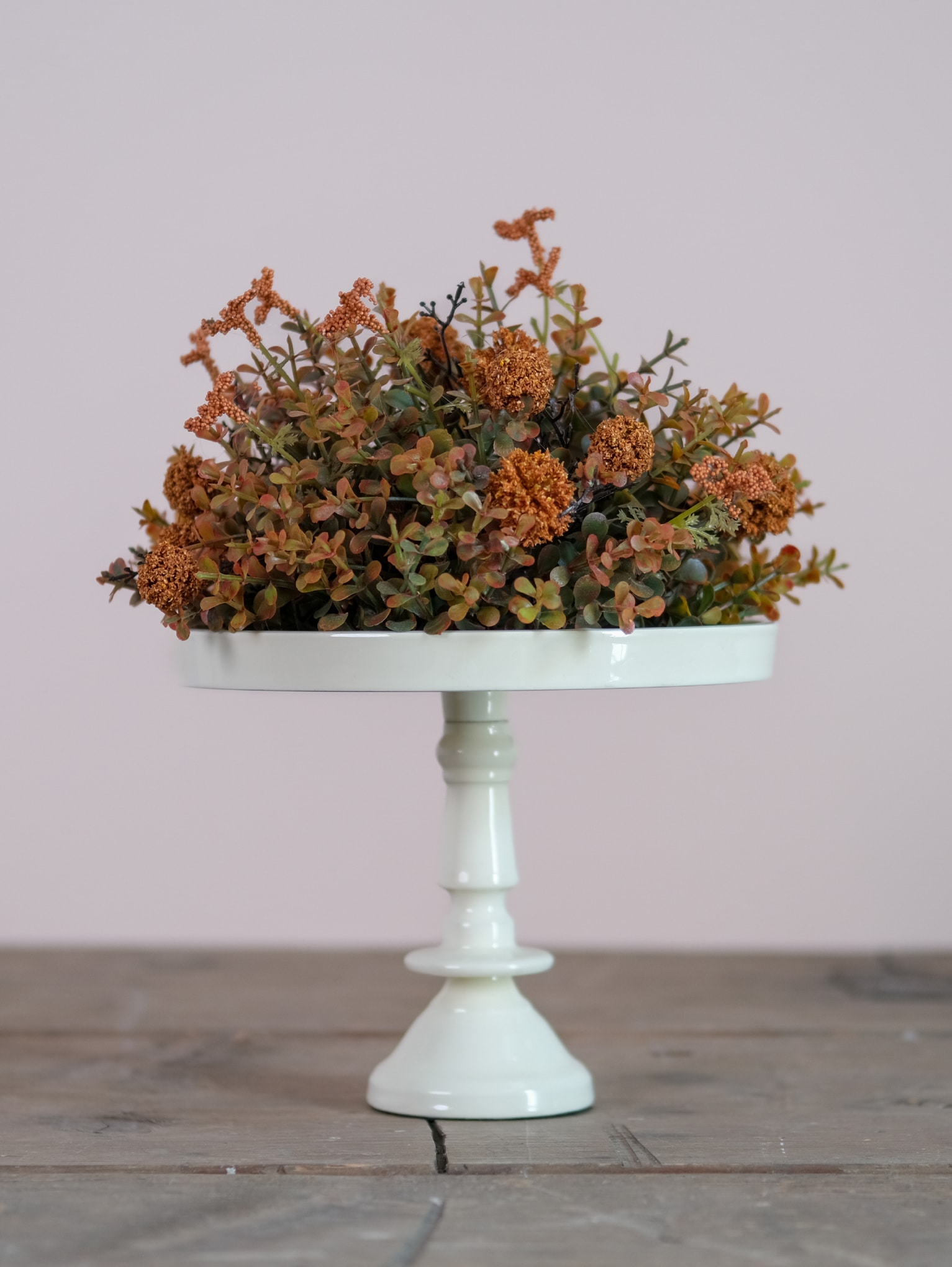 Off-white enamel pedestal stand with dried floral arrangement, styled on rustic wood surface
