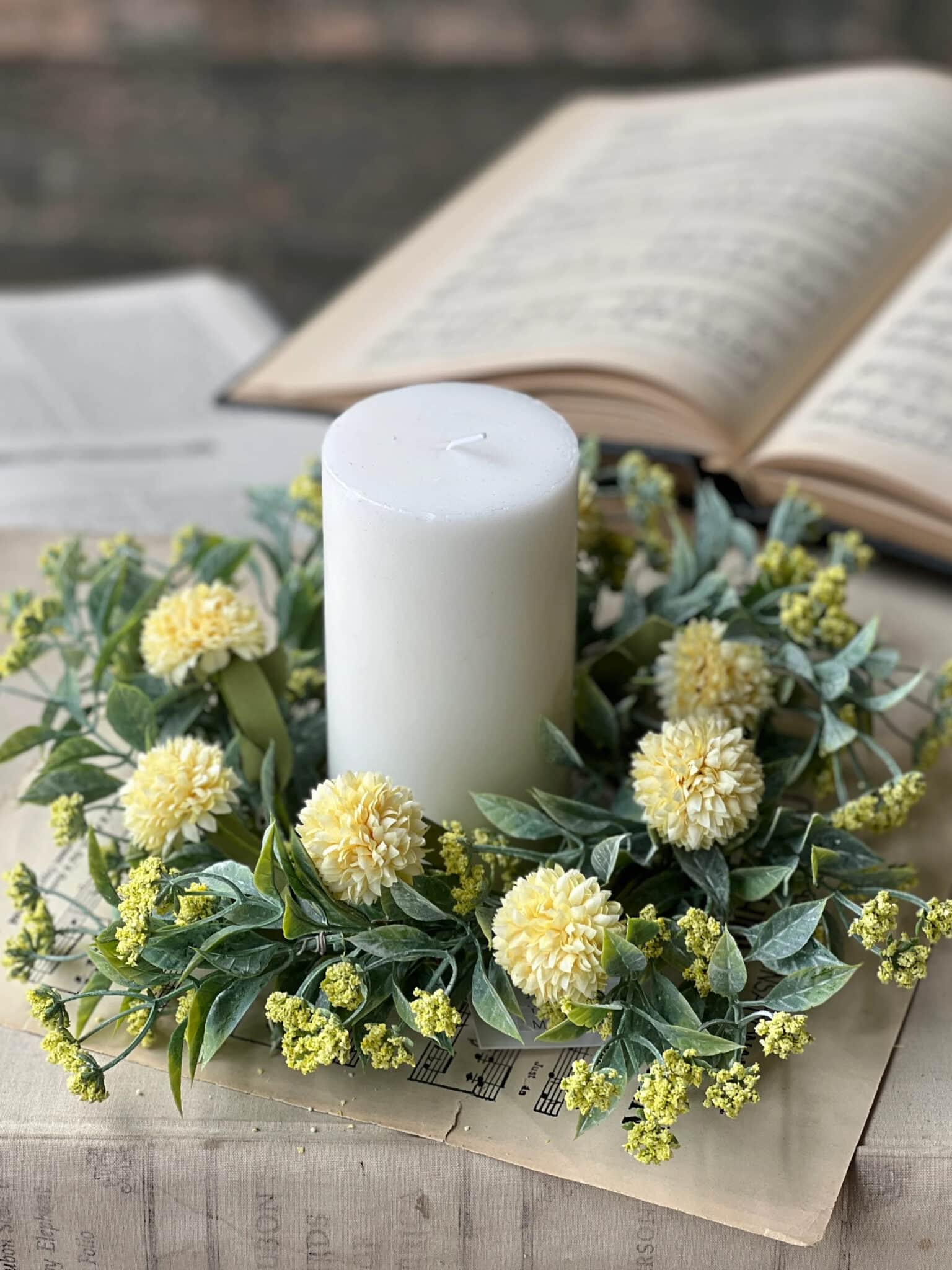be-made-hays-ks-yellow-garden-pom-candle-ring-with-pillar-candle Yellow Garden Pom Candle Ring styled around a white pillar candle with mixed greenery.