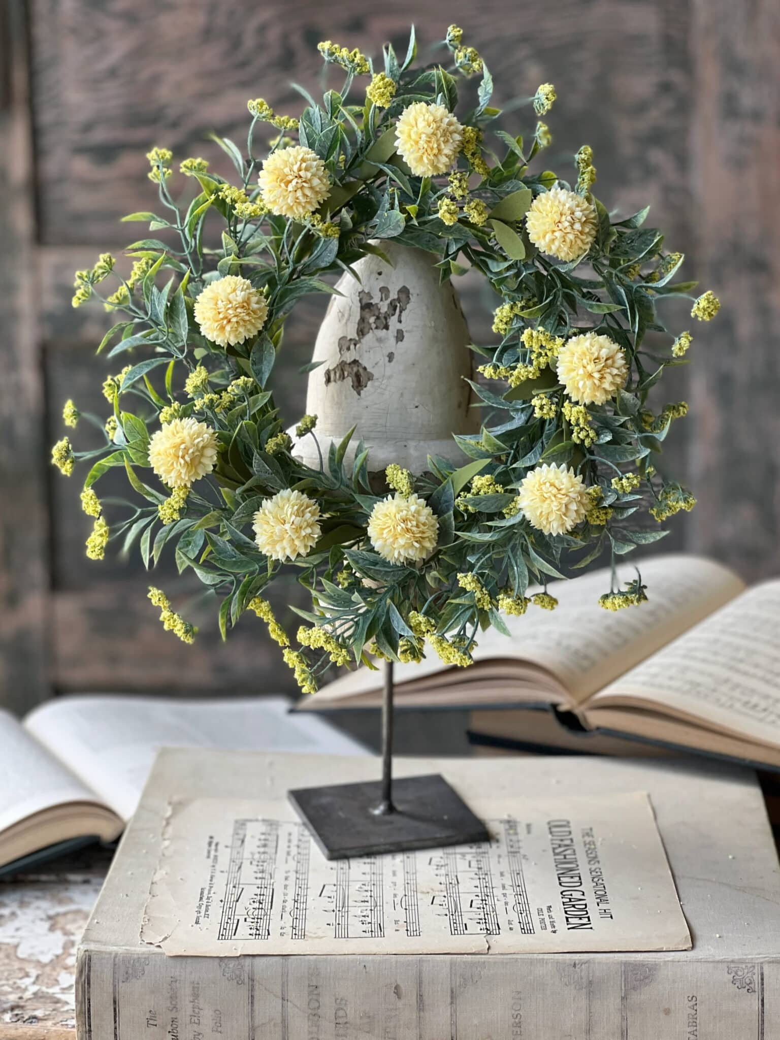 Yellow Garden Pom Candle Ring displayed on a stand with soft yellow blooms and realistic foliage.