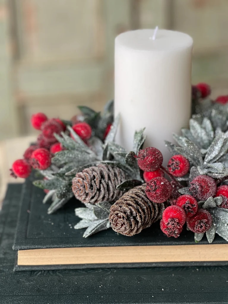 Close-up of frosted pine cones and sugared red berries arranged with icy laurel leaves around a white candle.