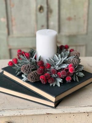 Frosted Berry Candle Ring with icy leaves and pine cones displayed on stacked vintage books with a white candle.