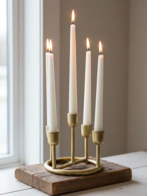 Gold aluminum multi taper candle holder with five staggered holders and white taper candles, styled on a rustic wood block near a window.
