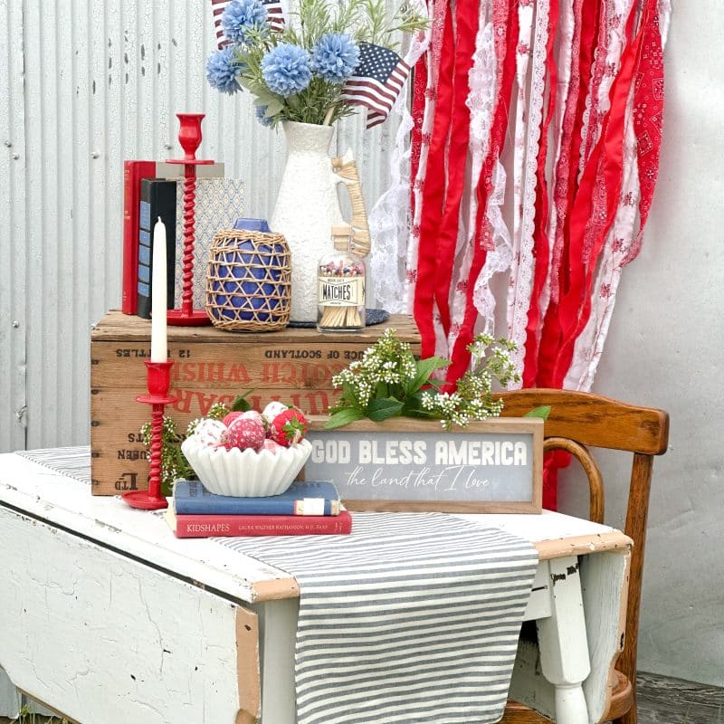 Side angle of styled scene with vintage-inspired red, white, and blue home decor on a rustic table