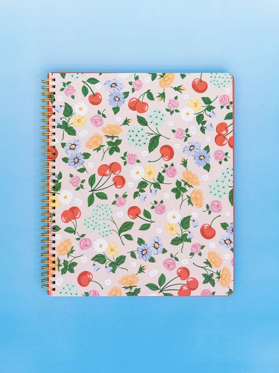 Notebook with floral and cherry design displayed on a bright blue background.