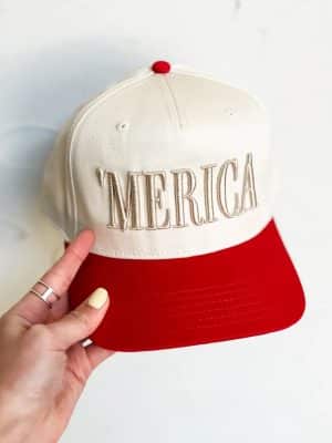 Close-up of red and natural two-tone trucker hat with puff-embroidered 'MERICA lettering.