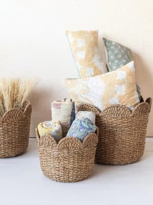 Set of natural handwoven scalloped-edge baskets filled with patterned pillows and rolled textiles.