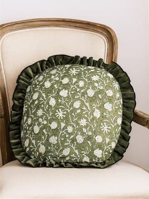 Green round floral block print pillow with ruffled edge on a cream upholstered chair.
