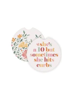 Round ceramic car coasters featuring the quote โSheโs a 10 but sometimes she hits curbsโ with a colorful retro font and floral pattern on the back.
