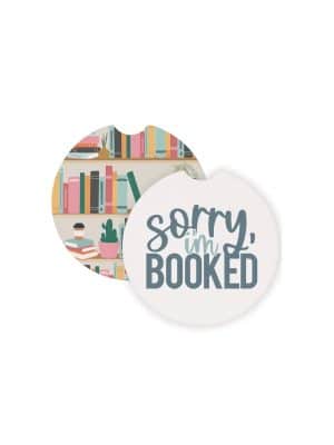 Round ceramic car coasters featuring a bookshelf illustration and the phrase “Sorry, I’m Booked,” designed to fit in standard car cup holders.