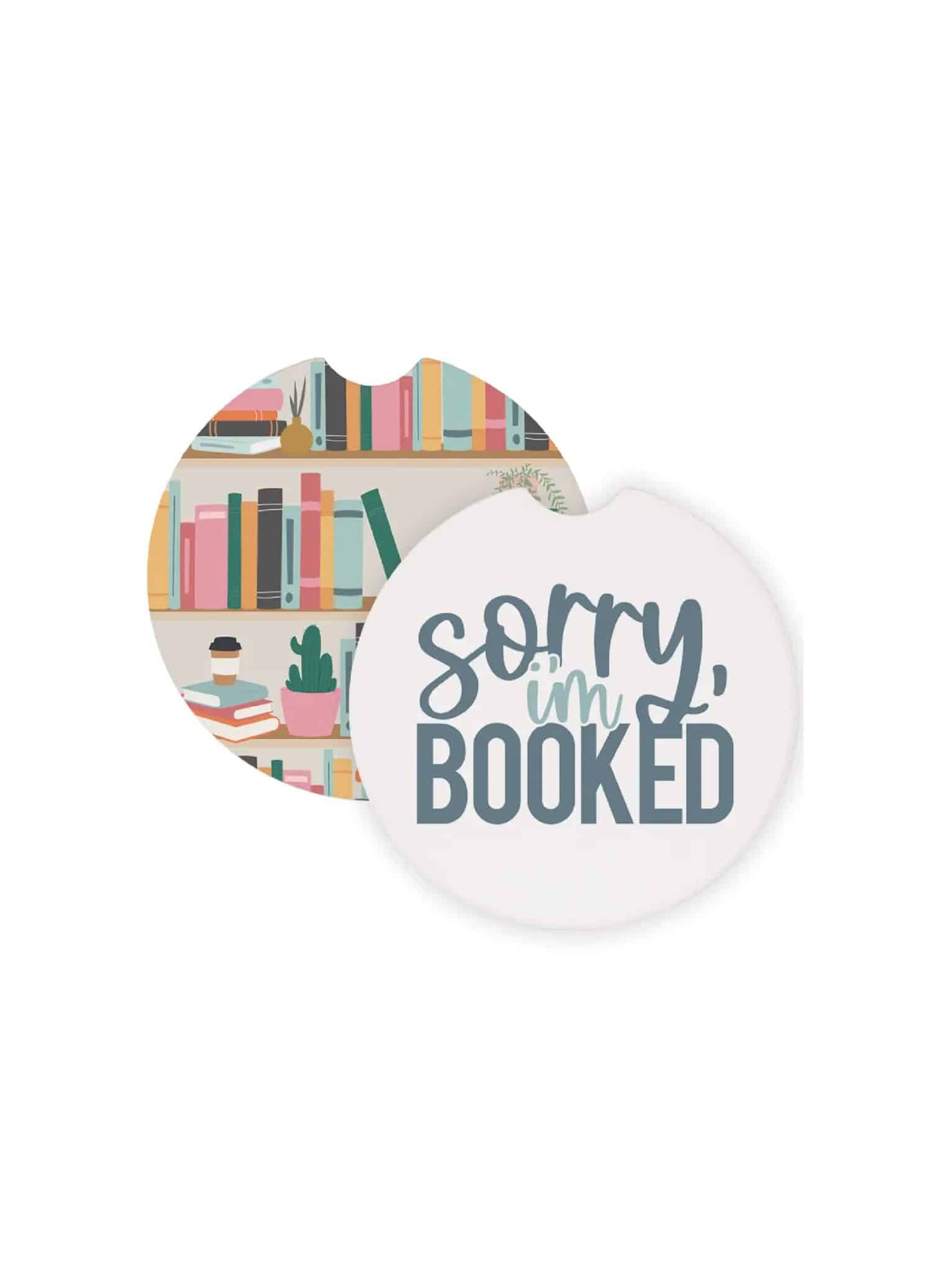 be-made-hays-ks-sorry-im-booked-car-coasters Round ceramic car coasters featuring a bookshelf illustration and the phrase “Sorry, I’m Booked,” designed to fit in standard car cup holders.