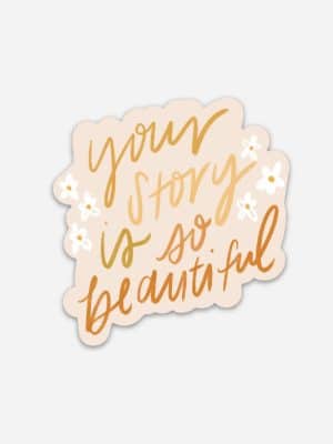Encouraging vinyl sticker with the phrase “your story is so beautiful” in gold script with small white flowers.