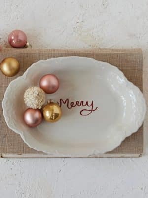 Stoneware “Merry” platter styled with pink and gold ornaments on a neutral surface.