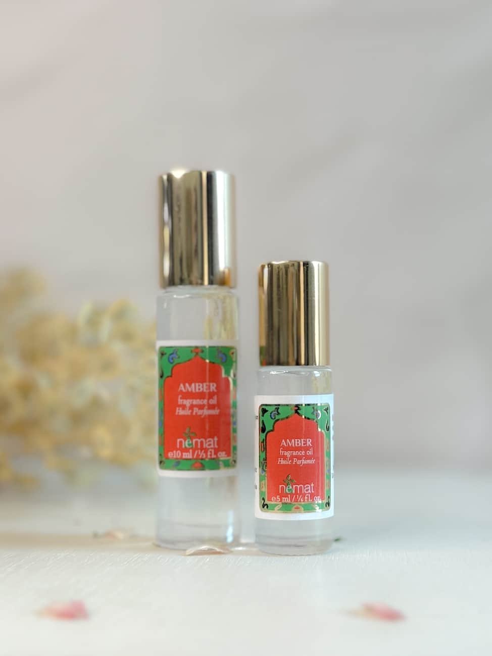Two bottles of Nemat Amber Roll-On Perfume Oil—one full-size and one mini—displayed with gold caps and decorative red-and-green labels