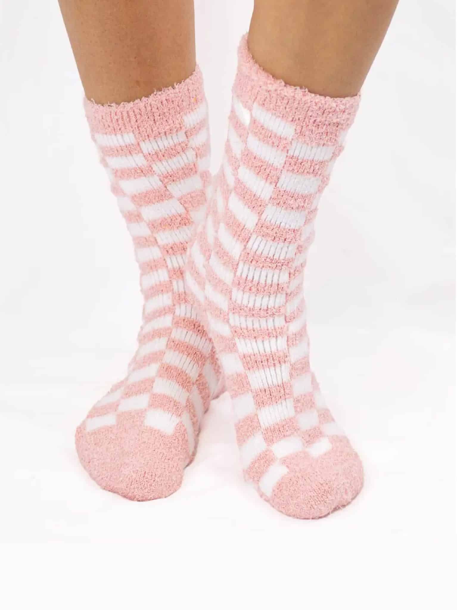 Pink and white checkered fuzzy socks worn on feet, showing the soft plush texture and snug fit.