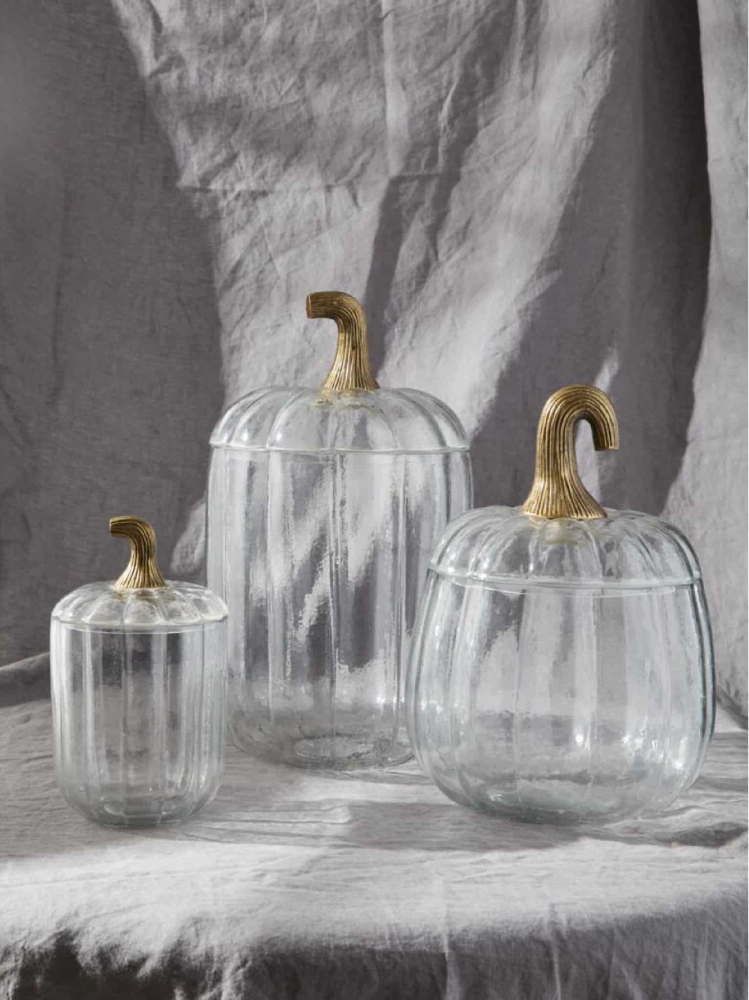 Three clear glass pumpkins with antique bronze lids displayed on a neutral backdrop