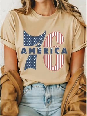 Tan t-shirt with 1776 America stars and stripes graphic, worn with light denim and a brown jacket.