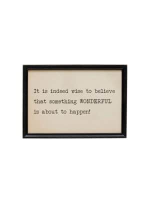 Black-framed wooden sign with the quote “It is indeed wise to believe that something wonderful is about to happen!” printed in vintage typewriter-style font on a cream background.