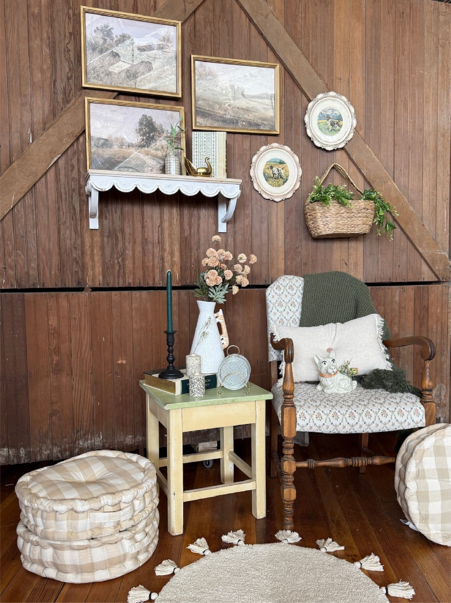 Moody moments corner with vintage frames, decorative dog plates, hanging basket with greenery, black empire candle holder, bud vases, onion sprays, rattan vase, checkered cushions, tufted armchair, and tassel rug.