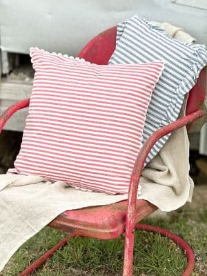 Red ticking stripe scallop pillow layered with a blue stripe ruffle pillow on a vintage red metal chair with natural table runner.