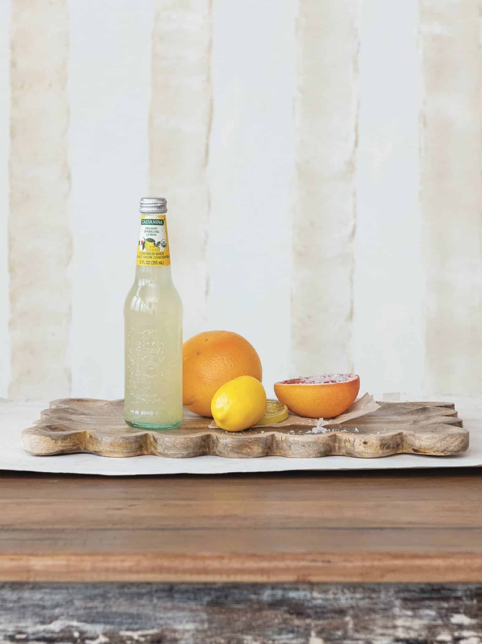 Scalloped mango wood tray styled with citrus and a bottle on a rustic table.