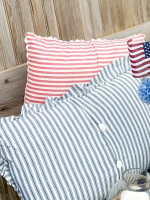 Blue ticking stripe pillow with button closure and ruffle edge layered in front of a red and white scalloped-edge stripe pillow.