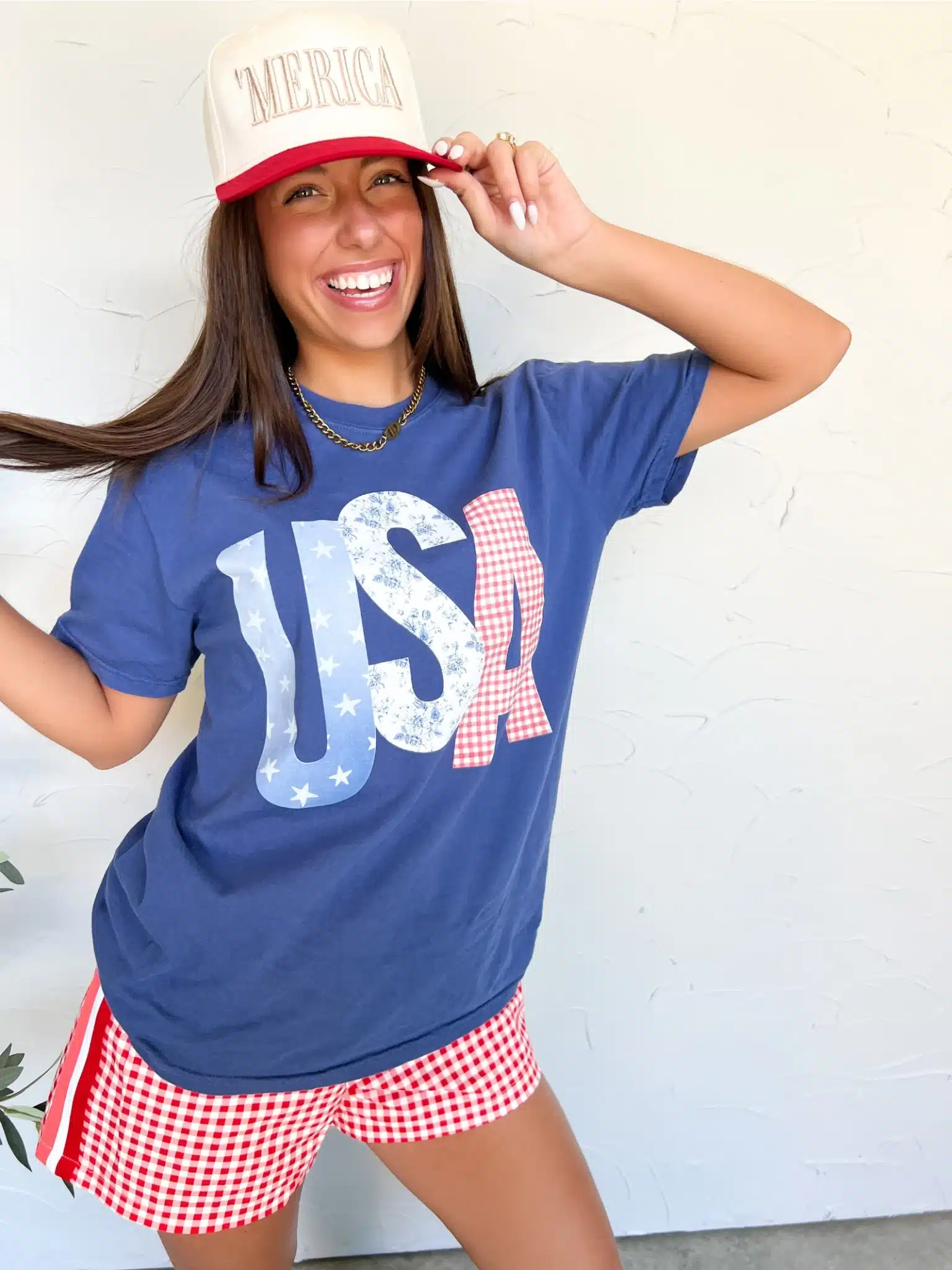 Woman wearing USA Patchwork Tee in China Blue and 'MERICA embroidered trucker hat in red and natural, styled for the 4th of July.