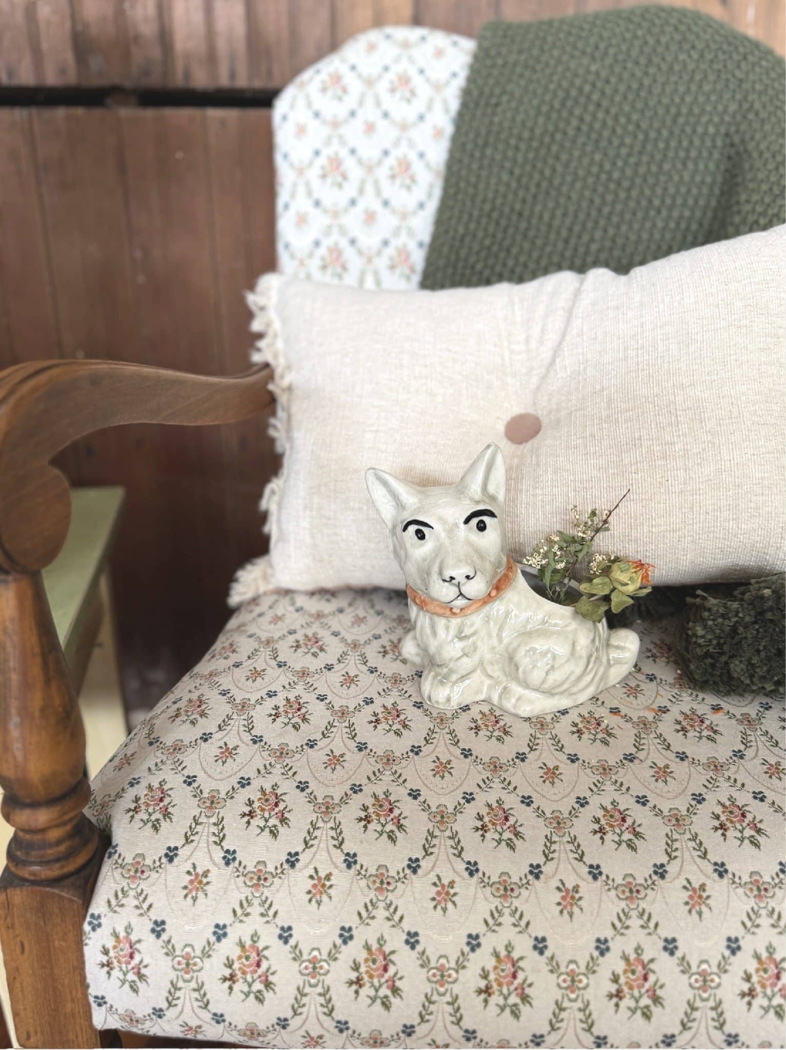 White ceramic scotty dog planter styled with dried florals, sitting in front of a neutral tufted pillow and green knit blanket.