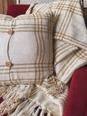 The Plaid Woven Wheat Throw Pillow adds soft texture and simple charm to any room. Its warm cream base and wheat-colored plaid lines create a cozy, classic look. The reversible cover and wooden button-style closures give it a sweet, homespun touch. Style it on a sofa, bed, or accent chair. It also pairs perfectly with our matching Plaid Woven Wheat Throw Blanket. The look is easy, neutral, and made for farmhouse, cottage, or modern natural decor. This pillow is comfortable, versatile, and beautiful for year-round use. Material: 100% cotton cover with polyester fill Details: Removable cover for easy cleaning Dimensions: 18″ x 18″