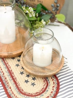 Close-up of small wood and glass hurricane candle holder with white candle on striped and star-spangled table runners