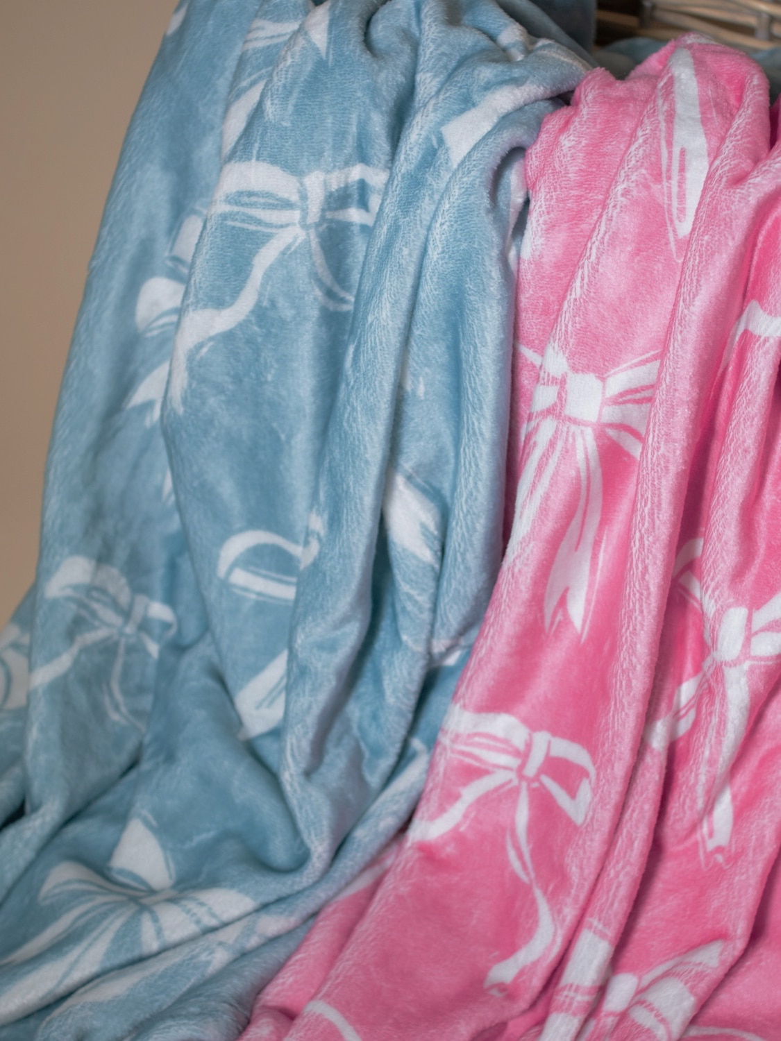 Light blue and pink bow-patterned throw blankets draped together over a woven basket, highlighting soft texture and playful colors.