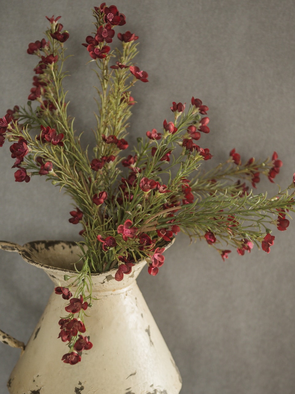 Burgundy Waxflower Spray arranged in a white pitcher vase with realistic greenery and blooms.