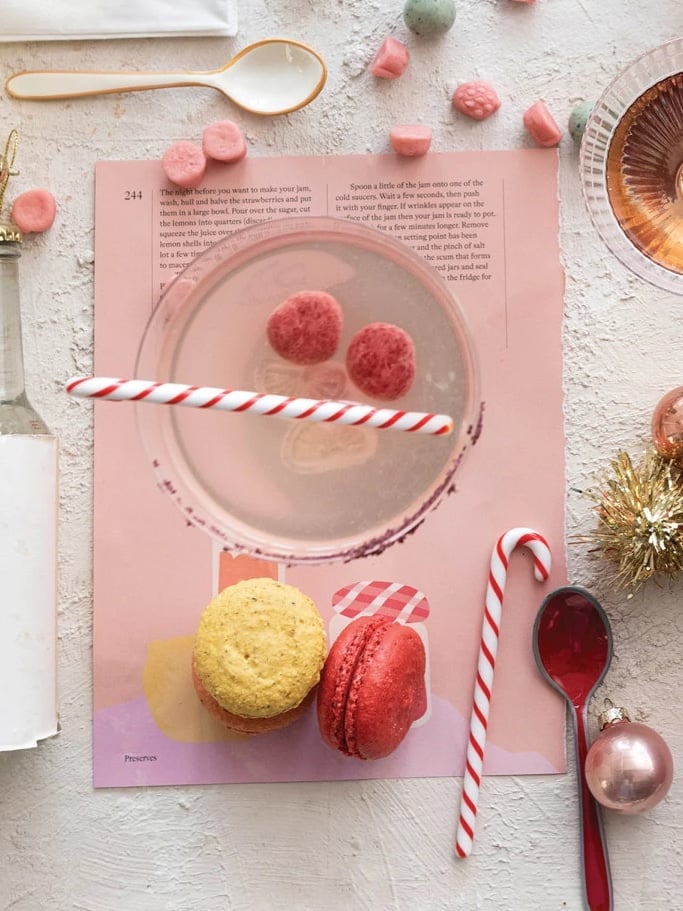 Flat lay of red and white Glass Candy Cane Stir Sticks styled with macarons, ornaments, and holiday table décor.