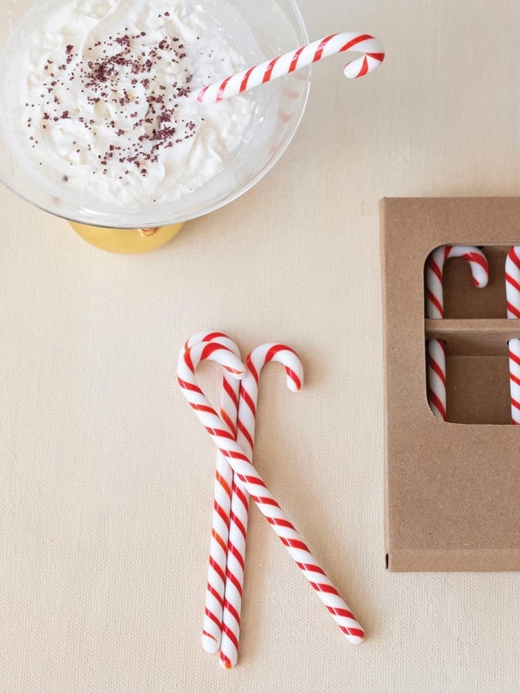 be-made-hays-ks-glass-candy-cane-stir-stick-holiday-gift Red and white Glass Candy Cane Stir Sticks shown beside a gift box and a bowl of whipped cream for festive holiday drinks.