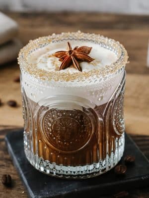 Clear retro arched drinking glass filled with a coffee cocktail topped with cream and star anise garnish.