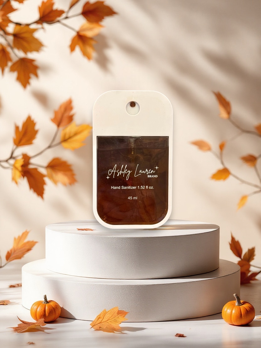 Crème Brûlée Hand Sanitizer Spray in sleek white case with dark brown liquid, styled with autumn leaves.