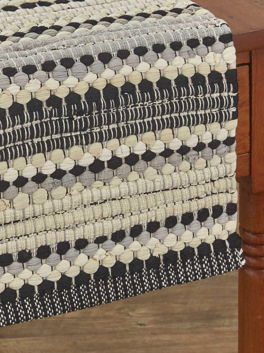 Close-up of black and white Chindi-style woven cotton table runner draped over wooden table edge.