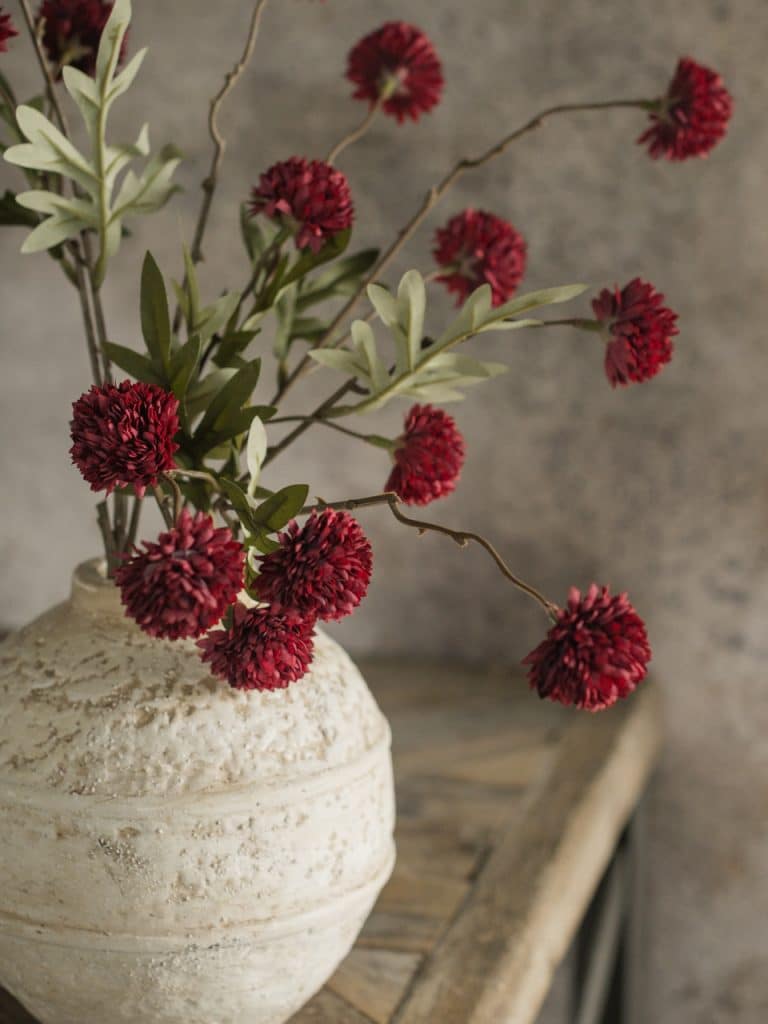 Dark Red Onion Spray styled in a textured white vase, showcasing layered red blooms and foliage.