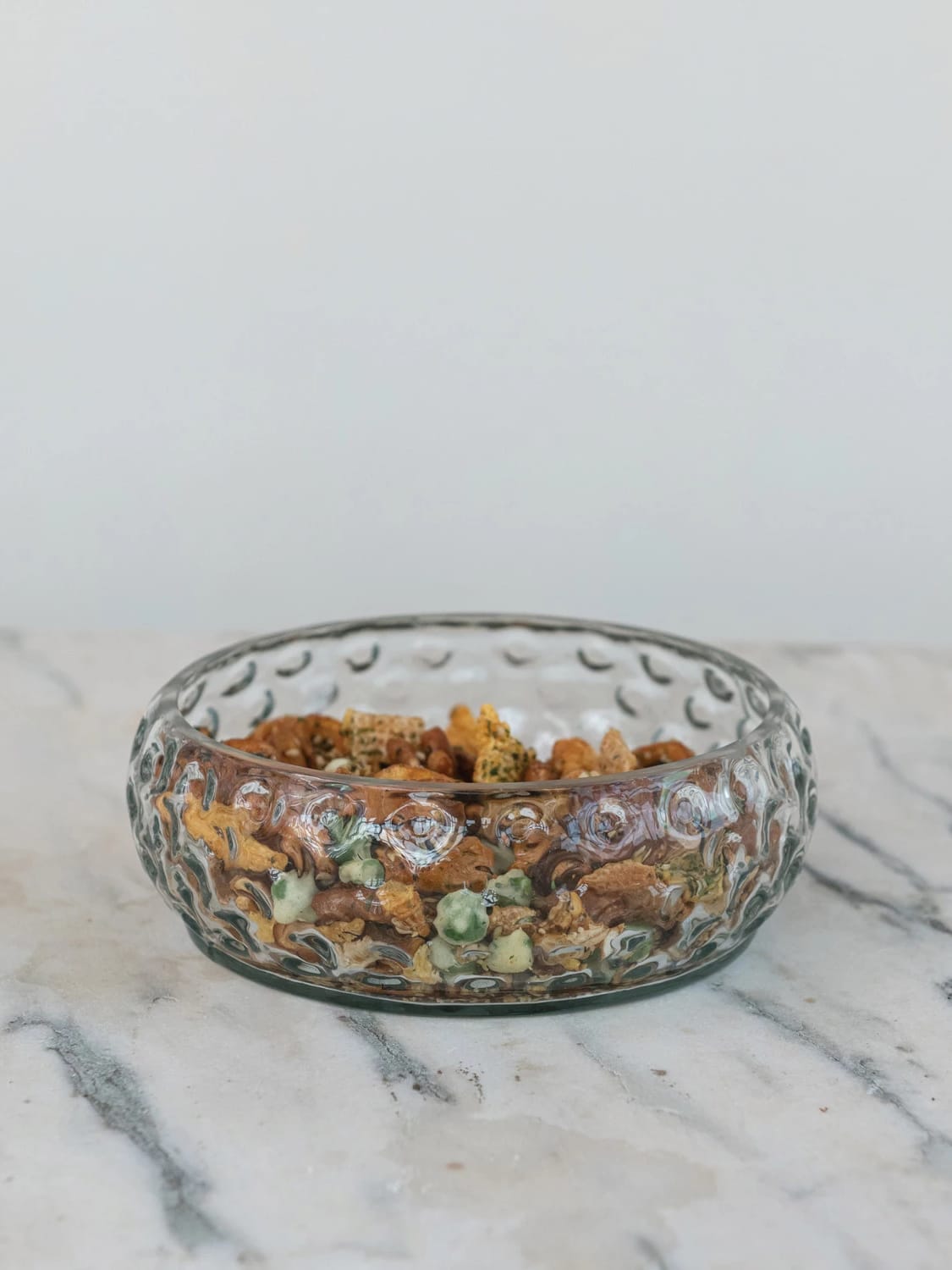Clear hand-blown hobnail glass bowl filled with snack mix displayed on marble surface.