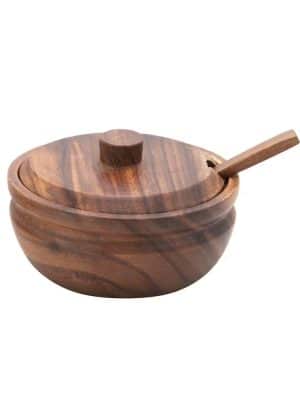 Side angle of round acacia wood bowl with matching lid and spoon tucked through the lid slot.